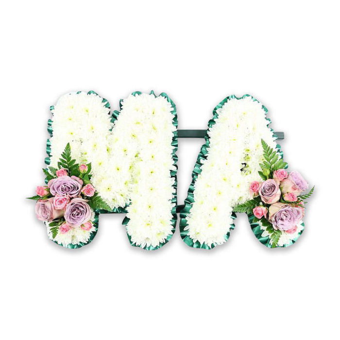 Set against a simple white backdrop, a floral tribute spelling the letters MA conveys both elegance and heartfelt sentiment, the kind often chosen to honour a mother or someone whose initials were M.A. Each capital letter is generously padded with pristine white chrysanthemums, arranged so closely that they form a smooth, plush surface with subtle undulations where the blossoms meet. The flowers catch the light softly, giving the tribute a calm, luminous quality, as though the letters are quietly glowing. Encircling both the M and the A is a neatly ruffled band of deep green ribbon, its satin sheen and pleated texture outlining each stroke with definition and poise. The ribbon's rich colour creates a striking but gentle contrast with the white petals, enhancing the clarity of the letters even from a distance. At the lower left foot of the M and the lower right foot of the A, symmetrical posies of pastel blooms create tender focal points. Here, soft-pink roses and muted lilac roses, accompanied by clusters of delicate pink spray roses, nestle among sprigs of fern and fresh greenery. Their petals appear velvety and layered, some fully open in generous spirals, others half-unfurled, lending depth and movement to the design. The tribute feels deeply personal, suitable for a funeral at a local Cranford church, a crematorium service near the Bath Road, or a farewell gathering after a wake in the neighbourhood. It reflects the thoughtful craftsmanship of an experienced Cranford florist, where traditional white funeral flowers are given a gentle, contemporary twist to express enduring love, peace, and gratitude for a life cherished and remembered.