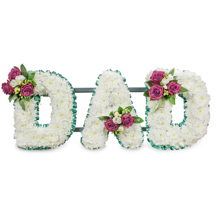 This lovingly made memorial lettering spells out DAD in three bold capital letters, each formed from a tight sea of small white chrysanthemums that give the piece a pillow-soft, immaculate texture. A pleated emerald-green ribbon crisply defines every contour, folding softly around the outer and inner edges to emphasise the clean lines against the white background. A subtle dark green or grey support bar links the letters and suggests a stable easel-ready structure for placement at a service. Strategic clusters of magenta roses - ranging from firm buds to gently unfurling blooms - are set with small white freesia and deep green leaves to punctuate the composition with colour and meaning. The first D bears its cluster on the upper left curve, the A's accent is tucked into the lower central V, and the last D mirrors the first with a corresponding cluster on the upper right arc, producing a harmonious and well-measured balance. The arrangement reads as an intimate message of remembrance: visually crisp yet softly expressive, with the cool green ribbon and the bright magenta providing a dignified warmth. Imagining it in the soft morning light of a chapel on Cranford High Street or laid near a favourite bench in Cranford Park helps place this tribute in local context; it is a classic choice for honoring a father, shaped with the kind of care an experienced local florist gives to bespoke funeral flowers.