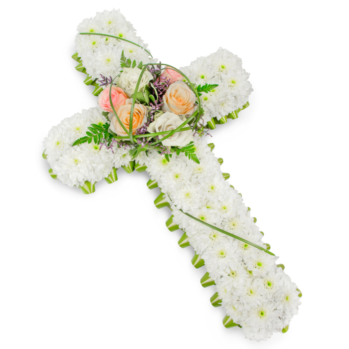 A traditional Christian cross made entirely from flowers is displayed on a bright white background, its form strong yet gentle in appearance. The main surface of the cross is tightly carpeted with countless small white chrysanthemums or similar round, cushiony blooms, each one contributing to a velvety, uniform texture that evokes purity and serenity. Running along the entire perimeter is a slim, precise band of vivid green foliage, the leaves forming a living frame that clearly defines every curve and angle of the cross's arms and base. The eye is naturally drawn to the raised cluster at the centre, where the vertical and horizontal sections meet. Here, several larger roses open in harmonious warm tones-soft peach, coral-tinged apricot, pale blush pink, and creamy white-creating a focal point that suggests gentle affection and loving memory. These roses are nestled into sprays of light, airy fern and a few looping strands of bright green grass, with fine hints of tiny purple flowers peeking through to add depth and textural contrast. The lighting is bright but soft, with no harsh shadows, so that each flower looks fresh and recently arranged, as if just prepared for delivery. This type of floral cross is a familiar sight at funerals and memorial services around Cranford, whether placed beside the coffin, at the front of a church, or laid respectfully at a graveside. It embodies a message of faith, peace, and enduring connection, reflecting the careful craftsmanship and understanding of loss that local Cranford florists bring to their funeral tributes.