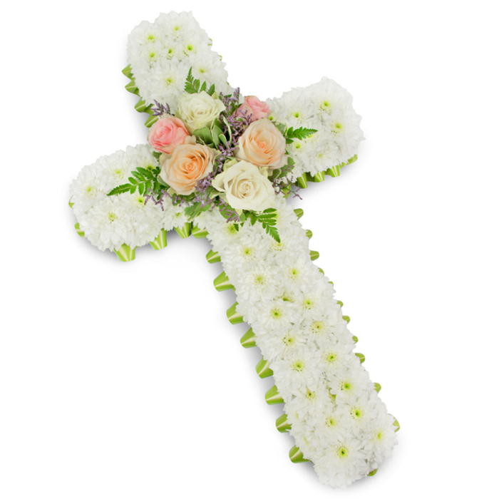 A traditional Christian cross made of flowers is presented on a pristine white background, the image lit so evenly that every petal and texture is clearly visible, while a faint drop shadow lifts the tribute forward. The body of the cross is entirely blanketed with tightly packed white button chrysanthemums, their small, rounded faces arranged edge to edge to form a thick, luxurious layer of bloom. This uniform spread of white gives the cross a soft, quilted appearance, suggesting purity, reconciliation, and the gentle hush of a quiet chapel. Running along the outer rim of the cross, a slim band of lime green ribbon appears like a fine border, just visible beneath the chrysanthemums, outlining each arm and adding a precise, almost tailored edge to the design. At the central intersection, a compact spray of roses introduces subtle colour and emotional warmth. Several open blooms in creamy white, delicate blush pink, and light peach or apricot are carefully grouped together, their petals unfolding gracefully from tight centres into full, rounded shapes. Wisps of feathery green fern and short stems of lilac or pale lavender filler flowers are woven among the roses, providing contrast in texture and tone while keeping the mood gentle and understated. The composition feels calm, balanced, and deeply respectful, the sort of funeral cross a local family in Cranford might place near the altar during a service or take to a grave in the peaceful surroundings of Cranford Park Cemetery. It reads as a clear expression of Christian faith and family love, crafted to honour a life with beauty, reverence, and a sense of enduring hope.