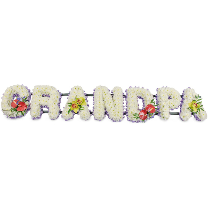 Displayed against a simple white background, this personalised funeral flower arrangement spells out GRANDPA in striking block capitals, arranged in a single, horizontal line as if resting on an invisible mantle. Each letter is clothed in a dense layer of pure white chrysanthemums, the small, tightly formed blooms packed closely together so their soft petals blend into a continuous, cloud-like texture. The whiteness suggests innocence, peace, and a sense of calm that often brings quiet comfort during a farewell. At the base of the letters, a narrow band of pale purple or lavender ribbon provides a graceful trim, just visible beneath the petals and adding a whisper of colour that helps each letter stand apart. A dark green framework runs behind the word, subtly holding the tribute together without drawing the eye from the flowers themselves. Four carefully placed clusters of accent flowers transform this from a simple word into a meaningful design: rich red anthuriums, with their heart-shaped, glossy spathes and upright spadices, are positioned on the 'G' and the 'D', where they stand out vividly against the white, symbolising deep love and remembrance. On the first and last 'A', sprays of yellow-green orchids, likely cymbidiums, unfold elegantly among fresh foliage, their luminous tones bringing a gentle, hopeful light. Designed in the style of bespoke tributes often chosen by families around Cranford, perhaps for services held near the local church or laid respectfully at a graveside, this arrangement captures both the strength and tenderness of a grandfather's role. It becomes a focal point of shared stories, expressing gratitude, affection, and the enduring bond between generations.