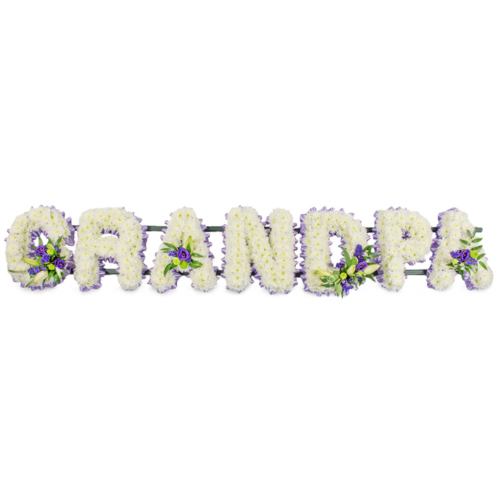 A lovingly composed funeral tribute spells out GRANDPA in large floral letters, arranged in a neat horizontal line as if resting gently on an invisible mantelpiece. Each block-style capital is generously coated in layers of small, fresh white chrysanthemums or carnations, their tightly clustered petals forming a thick, cushion-like surface that looks soft to the touch. The white flowers are immaculate and consistent from edge to edge, creating a calm, snowy field of texture that communicates sincerity, purity, and quiet respect. Sitting within this blanket of white, well-placed accents of rich purple blooms-likely lisianthus, statice, or small chrysanthemums-shine through like small jewels, accompanied by sprigs of lush green foliage. These accent sprays appear at key points: cupped within the curve of the G, nestled into the centre of the first A, highlighting the upright of the D, softening the bowl of the P, and lending a gentle flourish to the final A. The purple tones bring depth and solemn beauty, while the greenery adds an organic, garden-like touch. Beneath the letters, a dark green support rail or frame quietly holds everything together, mostly concealed by the mass of petals yet providing the stability needed for display at a funeral, memorial, or graveside gathering in and around Cranford, close to Bath Road and local churches. The tribute feels both traditional and personal, the kind of arrangement a family might choose when they want their grandfather's title lovingly written in flowers, offering comfort as they say goodbye and reflecting the dignity of a life well lived.