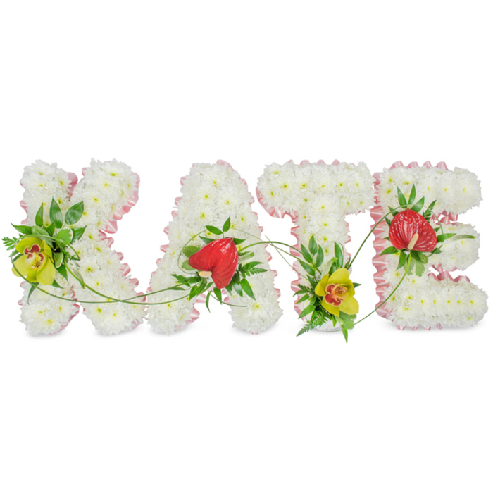 A beautifully detailed funeral tribute in the form of the name KATE stretches across a plain white background, each letter formed as a separate floral block yet designed to read as one unified gesture of remembrance. The letters are completely covered in close-knit white chrysanthemums, their small, rounded blooms pressed together to create a velvety blanket of petals. This dense, white surface gives the arrangement a calm, pure presence, like a soft cushion of flowers offered in sympathy. Trimming the outline of each letter is a narrow band of light pink ribbon, gently gathered and folded, which adds a delicate blush of colour and helps define the shapes. Along the left side of the K and tucked at the base of the T, lime-hued cymbidium orchids rise from clusters of dark, glossy greenery and airy fronds, their reddish-brown patterned throats adding subtle texture and interest. On the A and again on the E, bold red anthurium flowers with their characteristic heart form and smooth, waxy surfaces sit proudly among the white blooms, bringing a note of love and strength to the design. Slender green tendrils arc gracefully from one letter to the next, suggesting continuity, memory, and the way family ties stretch across time. The overall feeling is one of tenderness and quiet dignity, the kind of bespoke name tribute that might be chosen for a service in Cranford or carried gently to a resting place near Cranford Park or along Bath Road, created by florists who understand how important it is to reflect a life's story in flowers.