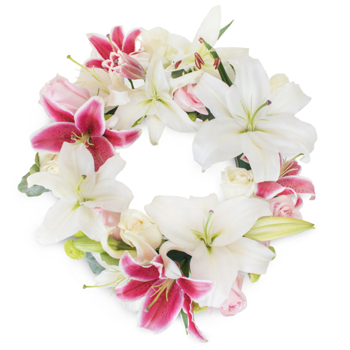 Against a spotless white backdrop, this vibrant circular floral wreath-expertly arranged by the skilled hands of Cranford Flowers-commands attention. Grand white lilies, their petals creamy and broad with delicate green pistils, radiate tranquility and purity, recalling the peaceful spaces of Cranford's gardens. Fuchsia pink stargazer lilies erupt with magenta intensity, delicately freckled at their centers, and provide a dramatic counterpoint throughout the circle. Interspersed among these statement blooms are soft, blush pink and ivory roses, some just budding, others full and ruffled, their gentle hues and textures lending romance and grace. Accents of muted green foliage, perhaps eucalyptus gathered from local sources, create subtle structure and offer fresh, earthy contrast. The wreath's circular design forms an unbroken ring of life, unity, and remembrance-richly symbolic for funeral or memorial services in Cranford. Isolated against the pristine background, the arrangement feels luminous and pure, each bloom's intricate details highlighted by the expert artistry of local florists. The result is a stunning floral tribute, timeless in its beauty and heartfelt in its message, available to bring comfort and honour throughout Cranford and its neighbouring communities.