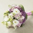 Resting on a subtle, creamy beige expanse, an artfully arranged bouquet bursts with joy and timeless charm-a signature floral design found only in Cranford. The bouquet's white Lisianthus blossoms are perfectly balanced between fully opened, cloud-like blooms and plump, delicate buds, their rich centers drawing you in. Among them, pastel pink and soft lavender Stock contribute a lightness, their softly frilled petals conjuring images of Cranford's flower-laden springtime pathways. Deep purple Allium orbs, bold and structural, punctuate the gentler hues with their distinctive star-shaped florets, while arching green leaves and emerald Lisianthus buds lend freshness and vitality. The composition is gently rounded with a natural elongation-a crafted harmony of movement and form. Binding the bouquet, a fuchsia pink satin ribbon spirals with a motif of petite pearls, creating a touch of refinement. Daylight bathes the scene, making every petal glow. True to Cranford's graceful aesthetic, this bouquet feels equally perfect as a wedding bouquet, table centerpiece, or heartfelt gift for a special occasion, sharing nature's beauty and a sense of anticipation that lingers long after the last petal falls.